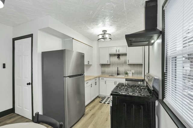 kitchen with appliances with stainless steel finishes, white cabinetry, sink, wall chimney range hood, and light hardwood / wood-style flooring