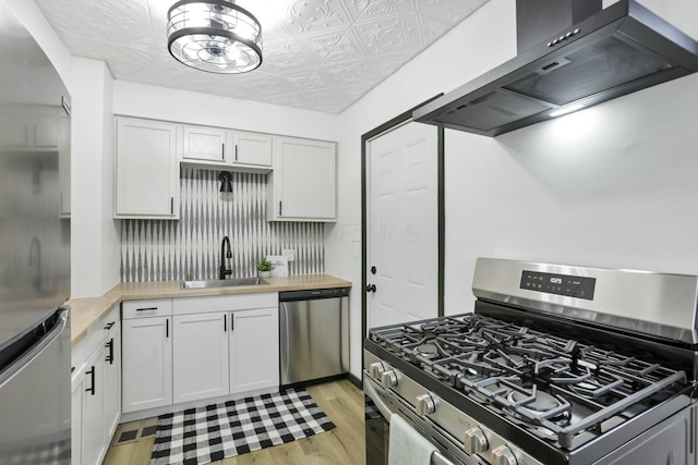 kitchen with sink, wall chimney range hood, wooden counters, white cabinetry, and stainless steel appliances