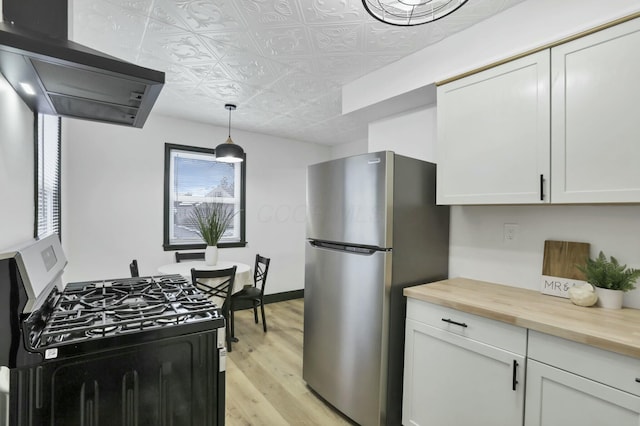 kitchen with hanging light fixtures, white cabinetry, appliances with stainless steel finishes, and butcher block counters