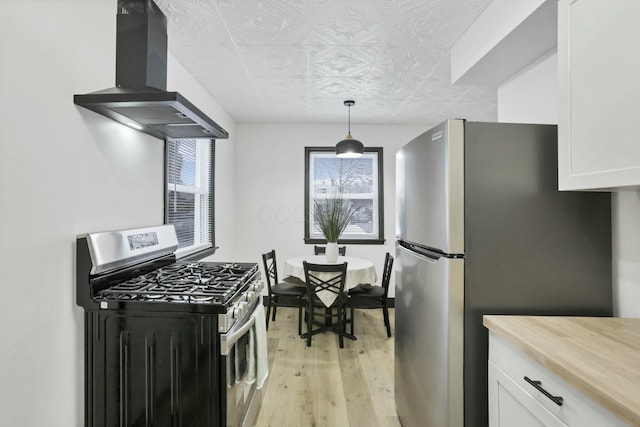 kitchen with white cabinetry, decorative light fixtures, ventilation hood, stainless steel appliances, and light hardwood / wood-style floors