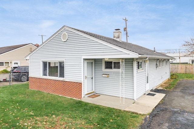 rear view of property with brick siding, a chimney, a yard, and fence