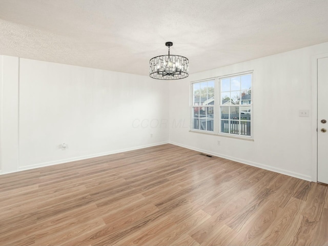 spare room with a notable chandelier, light wood-type flooring, and a textured ceiling