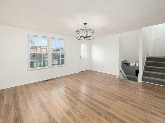 spare room with a chandelier, a textured ceiling, and light hardwood / wood-style flooring