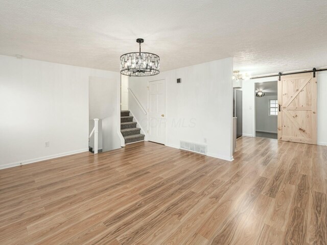 5006 Old Tree Ave, Columbus, OH 43228 - unfurnished room featuring a chandelier, light wood-style flooring, a barn door, a textured ceiling, and stairs