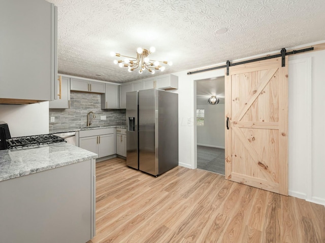 kitchen with a barn door, light wood-type flooring, sink, and appliances with stainless steel finishes