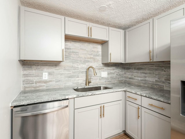 kitchen featuring light stone countertops, decorative backsplash, stainless steel dishwasher, a textured ceiling, and sink