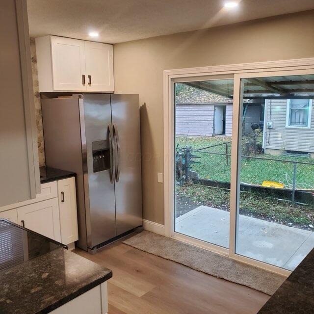 kitchen featuring white cabinets, stainless steel fridge with ice dispenser, light hardwood / wood-style flooring, and dark stone counters