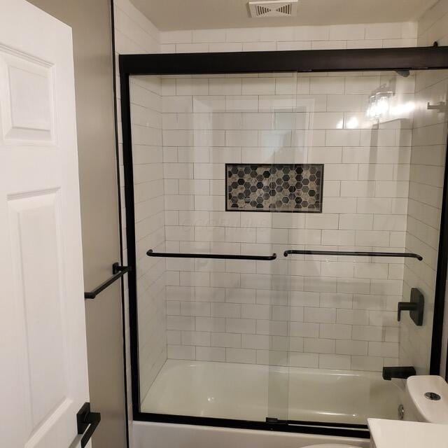 bathroom with toilet and combined bath / shower with glass door