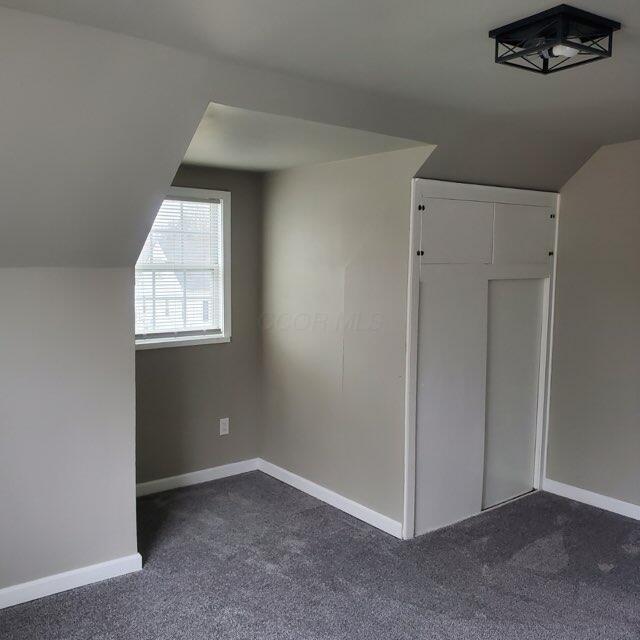 bonus room with dark carpet and vaulted ceiling