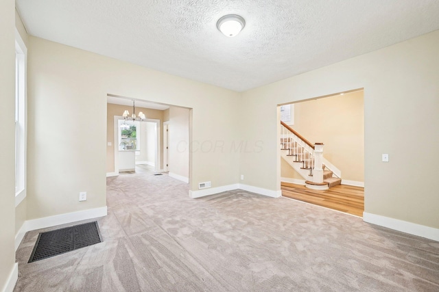 carpeted spare room with a textured ceiling and an inviting chandelier