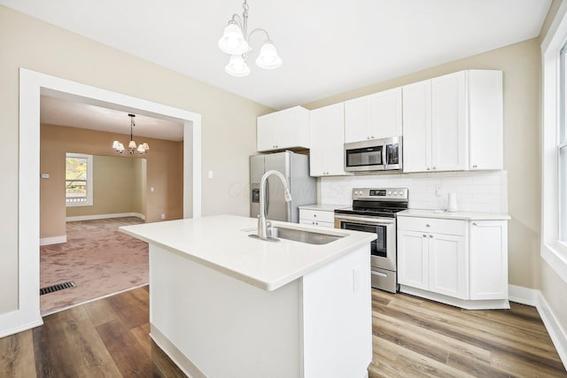 kitchen featuring white cabinets, sink, an island with sink, a notable chandelier, and stainless steel appliances