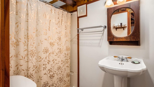 bathroom with beam ceiling, curtained shower, and toilet