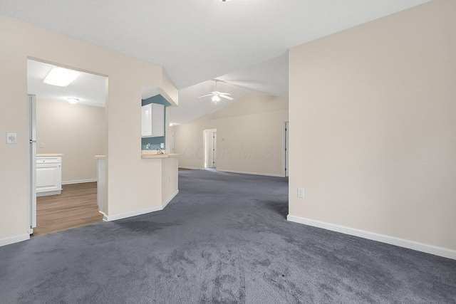 unfurnished living room featuring dark colored carpet, vaulted ceiling, and ceiling fan