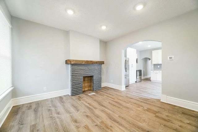 unfurnished living room featuring a fireplace, a textured ceiling, and light wood-type flooring