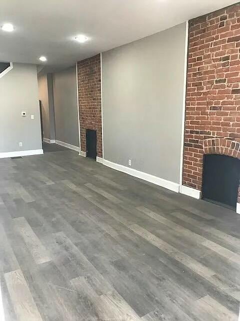 unfurnished living room featuring dark hardwood / wood-style flooring and a brick fireplace