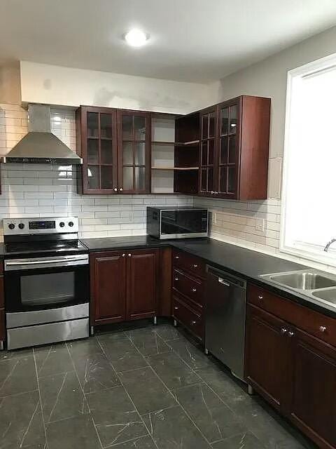 kitchen with decorative backsplash, sink, stainless steel appliances, and wall chimney range hood