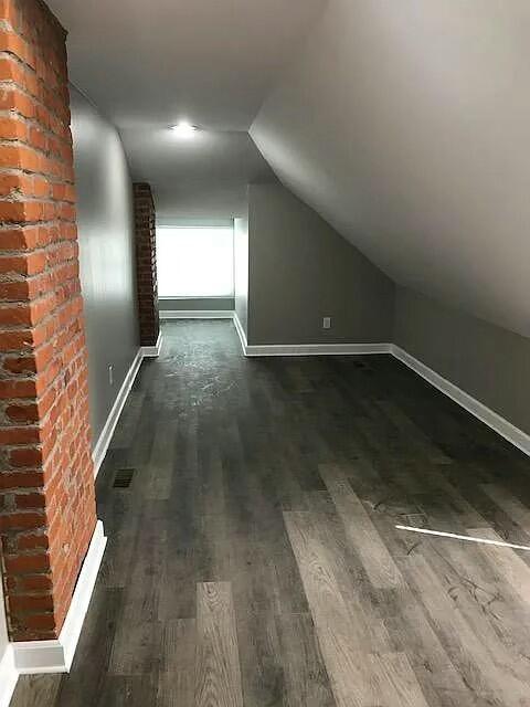 additional living space featuring dark wood-type flooring and vaulted ceiling