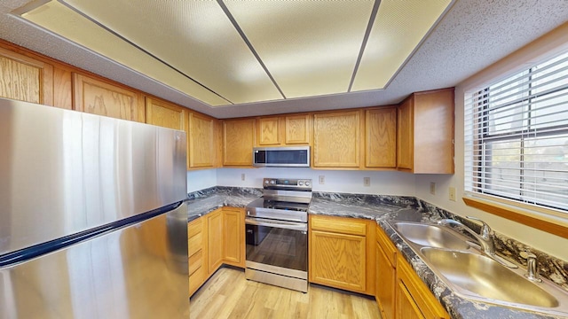 kitchen with sink, stainless steel appliances, a textured ceiling, and light wood-type flooring