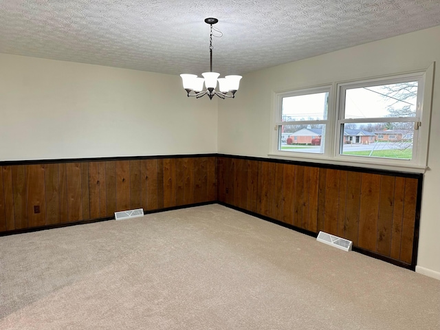 carpeted empty room featuring a textured ceiling, wooden walls, and a chandelier