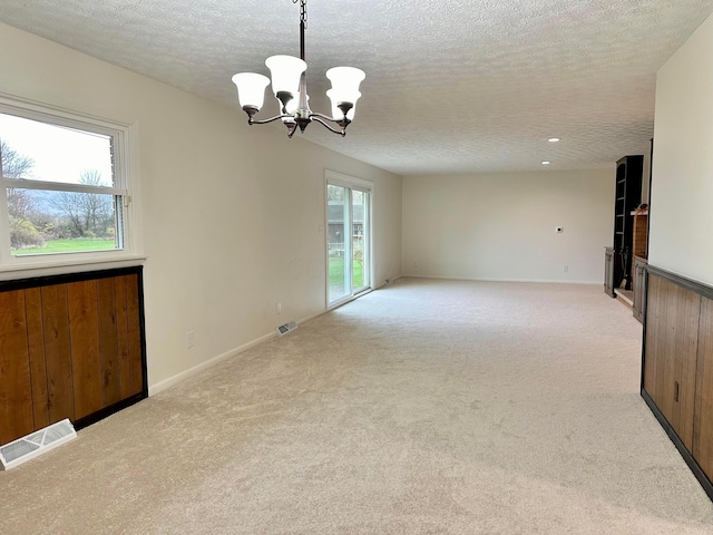 carpeted spare room with plenty of natural light, a textured ceiling, and a notable chandelier