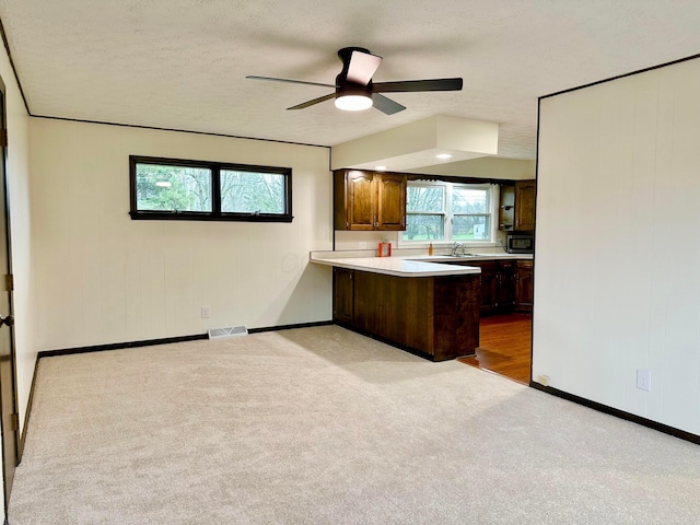 kitchen with light carpet, kitchen peninsula, ceiling fan, a textured ceiling, and dark brown cabinetry