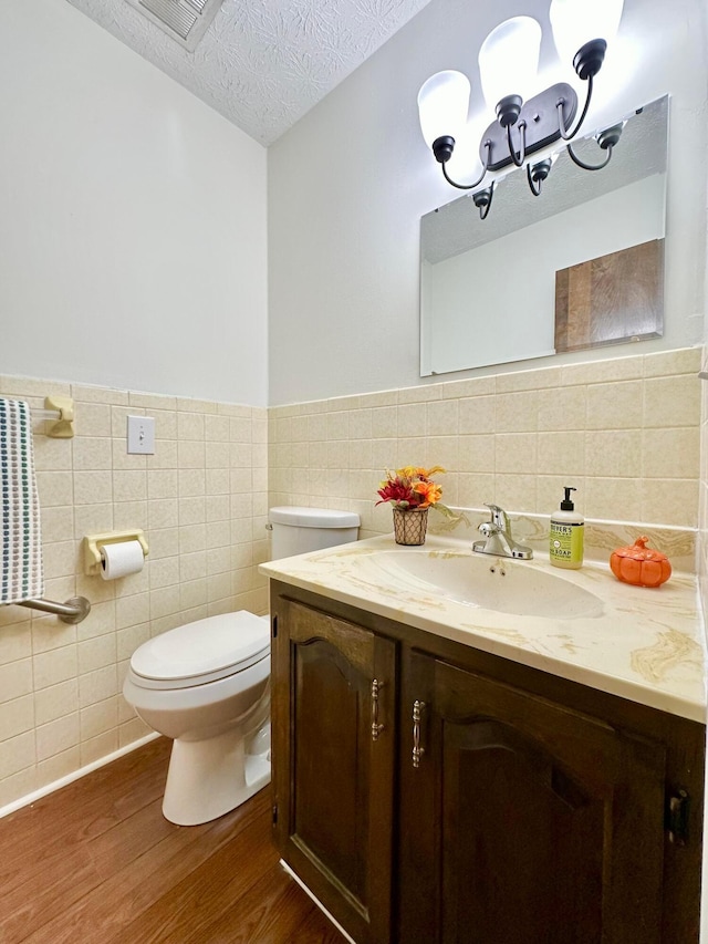 bathroom featuring vanity, a textured ceiling, hardwood / wood-style flooring, tile walls, and toilet