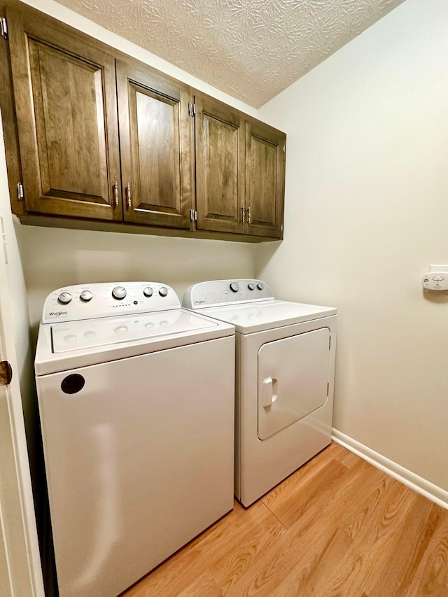 washroom with washing machine and dryer, light hardwood / wood-style flooring, cabinets, and a textured ceiling