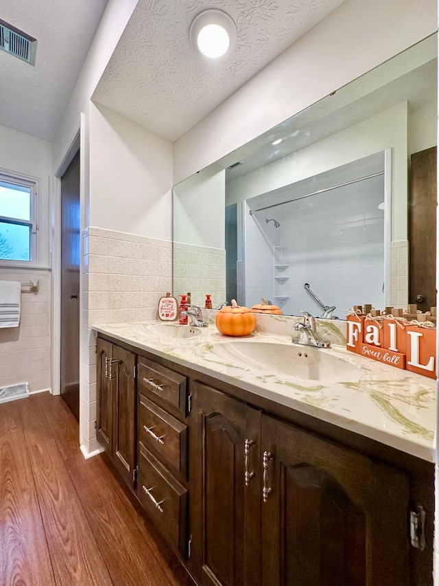 bathroom with hardwood / wood-style flooring, vanity, tile walls, and a textured ceiling