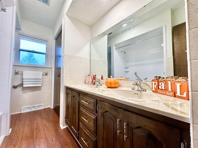 bathroom featuring hardwood / wood-style floors, vanity, tile walls, and a textured ceiling