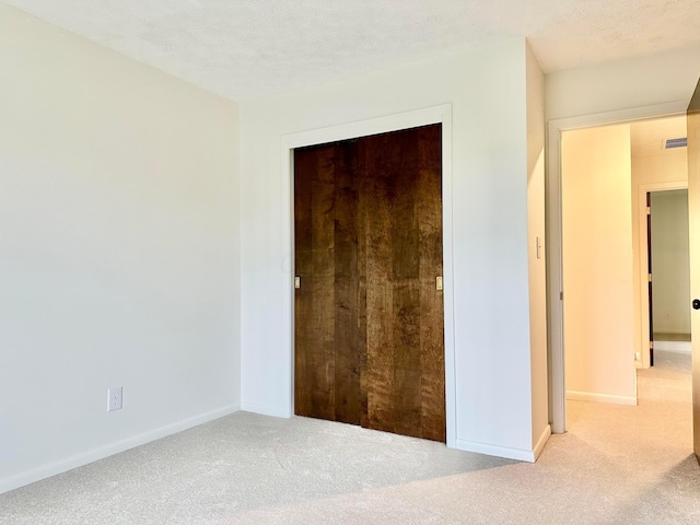 unfurnished bedroom featuring light colored carpet, a textured ceiling, and a closet