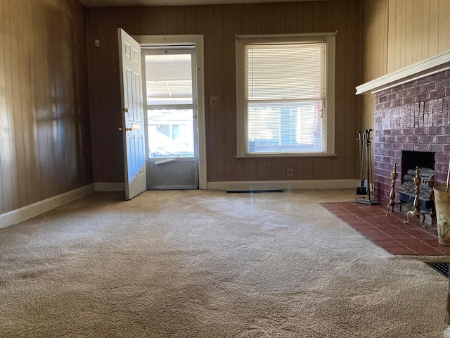 unfurnished living room with carpet flooring, wood walls, and a brick fireplace