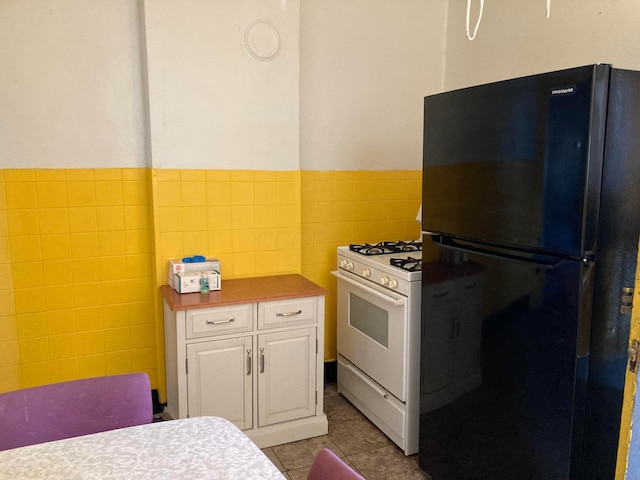 kitchen with black refrigerator, white gas range oven, light tile patterned floors, tile walls, and white cabinets