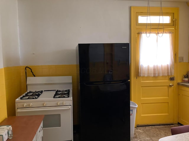 kitchen with light tile patterned floors, decorative light fixtures, black fridge, and gas range gas stove