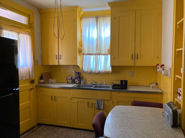 kitchen featuring pendant lighting, decorative backsplash, black refrigerator, and sink