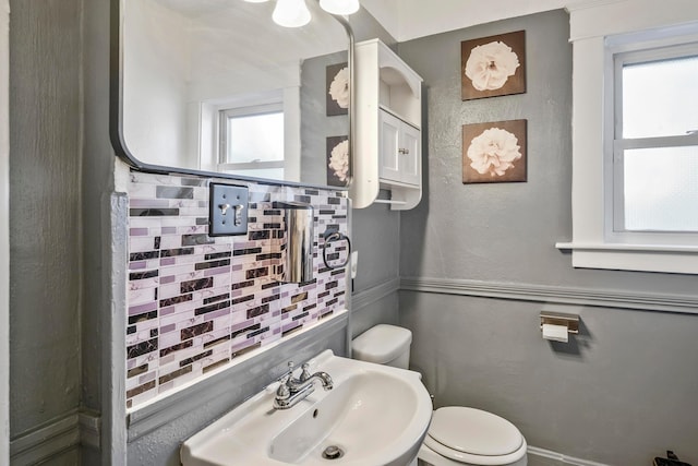 bathroom featuring decorative backsplash, toilet, sink, and a wealth of natural light