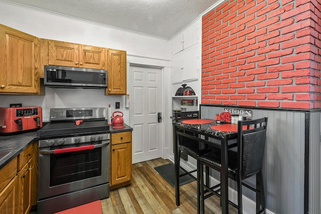 kitchen featuring crown molding, dark hardwood / wood-style floors, a textured ceiling, appliances with stainless steel finishes, and brick wall