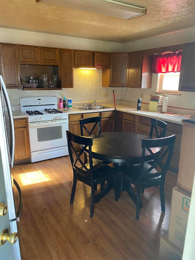 kitchen featuring hardwood / wood-style floors, sink, decorative backsplash, stainless steel fridge, and white gas stove