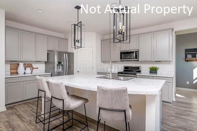 kitchen featuring sink, gray cabinets, a kitchen island with sink, stainless steel appliances, and decorative light fixtures