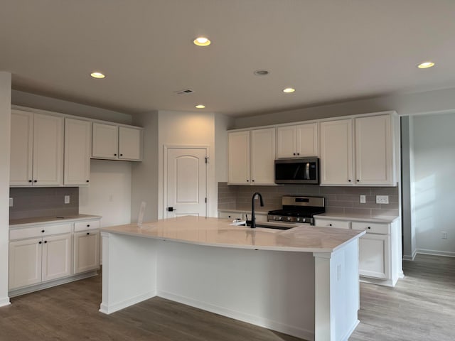 kitchen featuring an island with sink, wood-type flooring, sink, white cabinetry, and stainless steel appliances