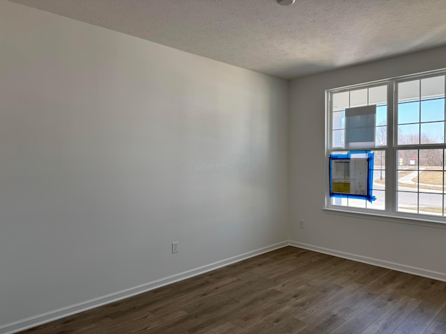 empty room with dark wood-style floors, baseboards, a wealth of natural light, and a textured ceiling