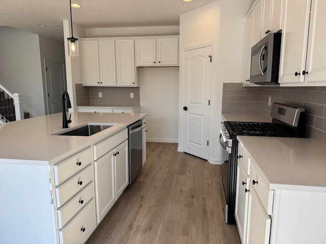 kitchen with a center island with sink, light wood finished floors, a sink, white cabinets, and appliances with stainless steel finishes