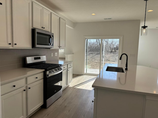 kitchen featuring a sink, backsplash, wood finished floors, appliances with stainless steel finishes, and light countertops