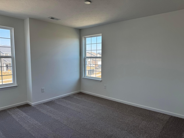 unfurnished room featuring visible vents, dark carpet, a textured ceiling, and baseboards