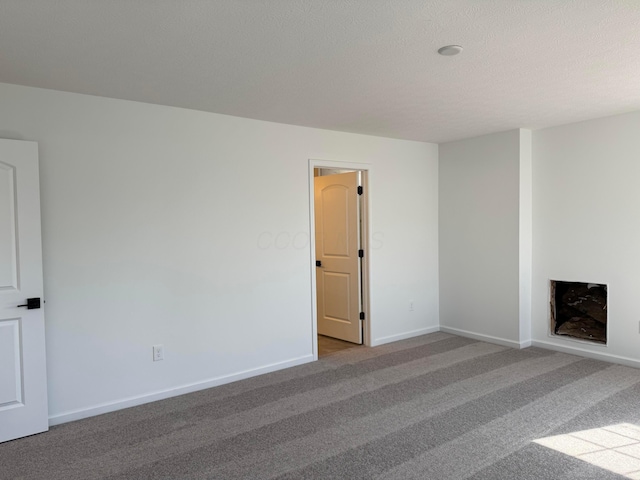 carpeted empty room with a fireplace, baseboards, and a textured ceiling