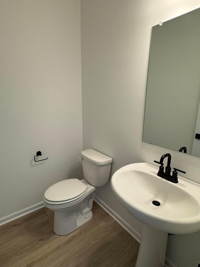 half bathroom with toilet, wood finished floors, baseboards, and a sink