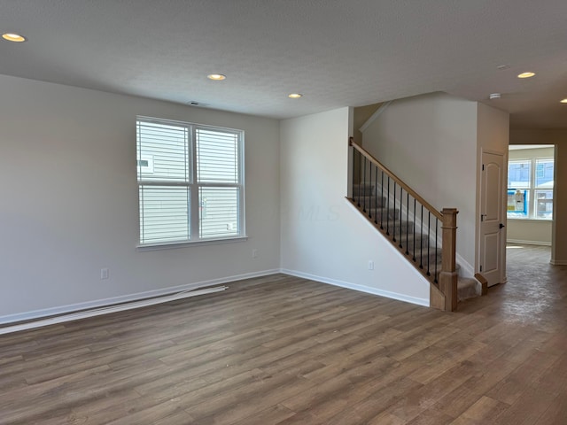 unfurnished room with recessed lighting, baseboards, wood finished floors, and stairs