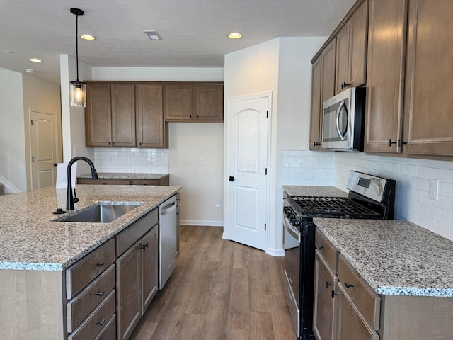 kitchen featuring a sink, light stone counters, appliances with stainless steel finishes, and dark wood-style floors