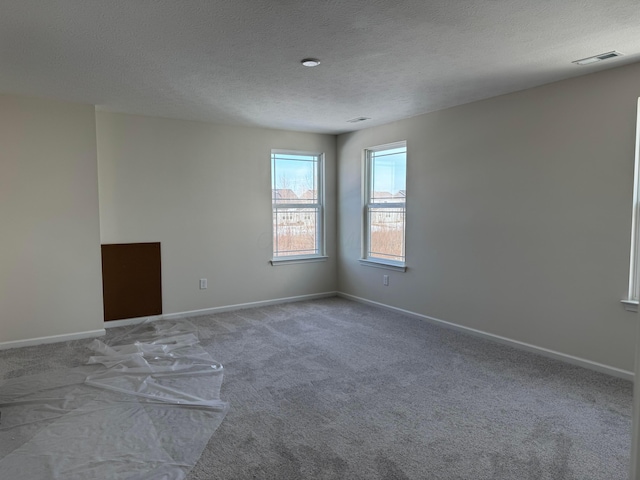 carpeted spare room with visible vents, a textured ceiling, and baseboards