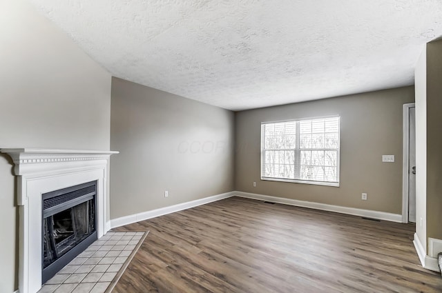 unfurnished living room with wood-type flooring, a tiled fireplace, and a textured ceiling