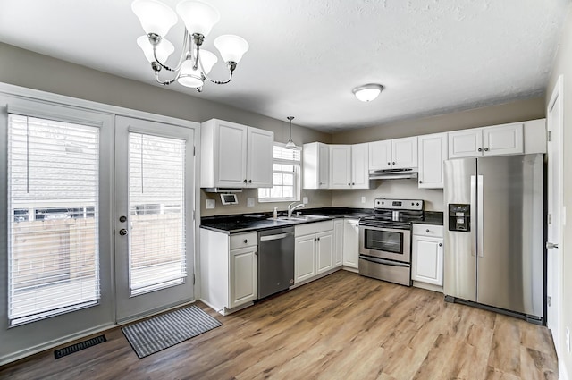 kitchen with pendant lighting, appliances with stainless steel finishes, a notable chandelier, light hardwood / wood-style floors, and white cabinets